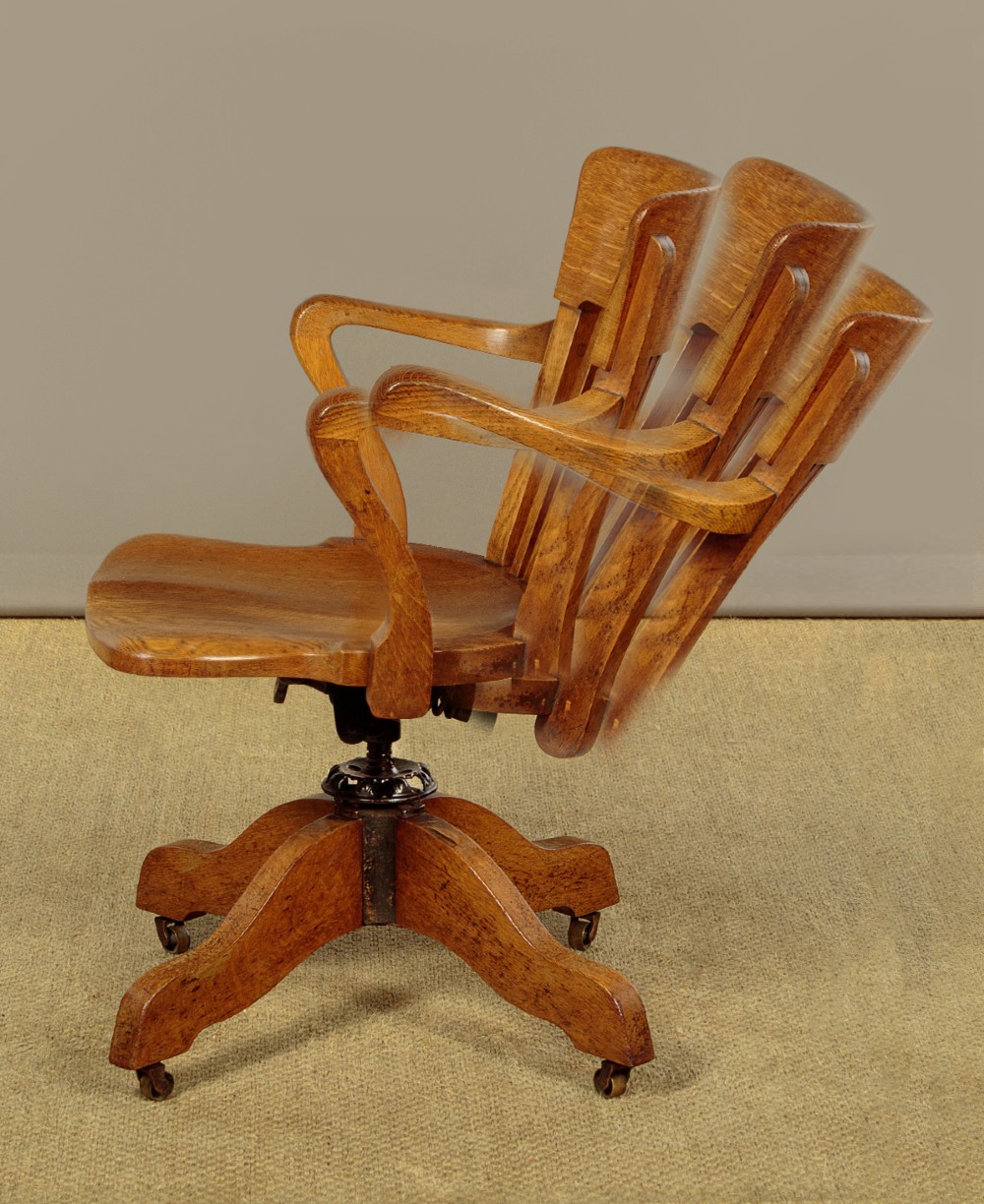 An early twentieth-century solid oak revolving desk chair featuring a slatted backrest, curved armrests, and a quadruped base on castors. View IV