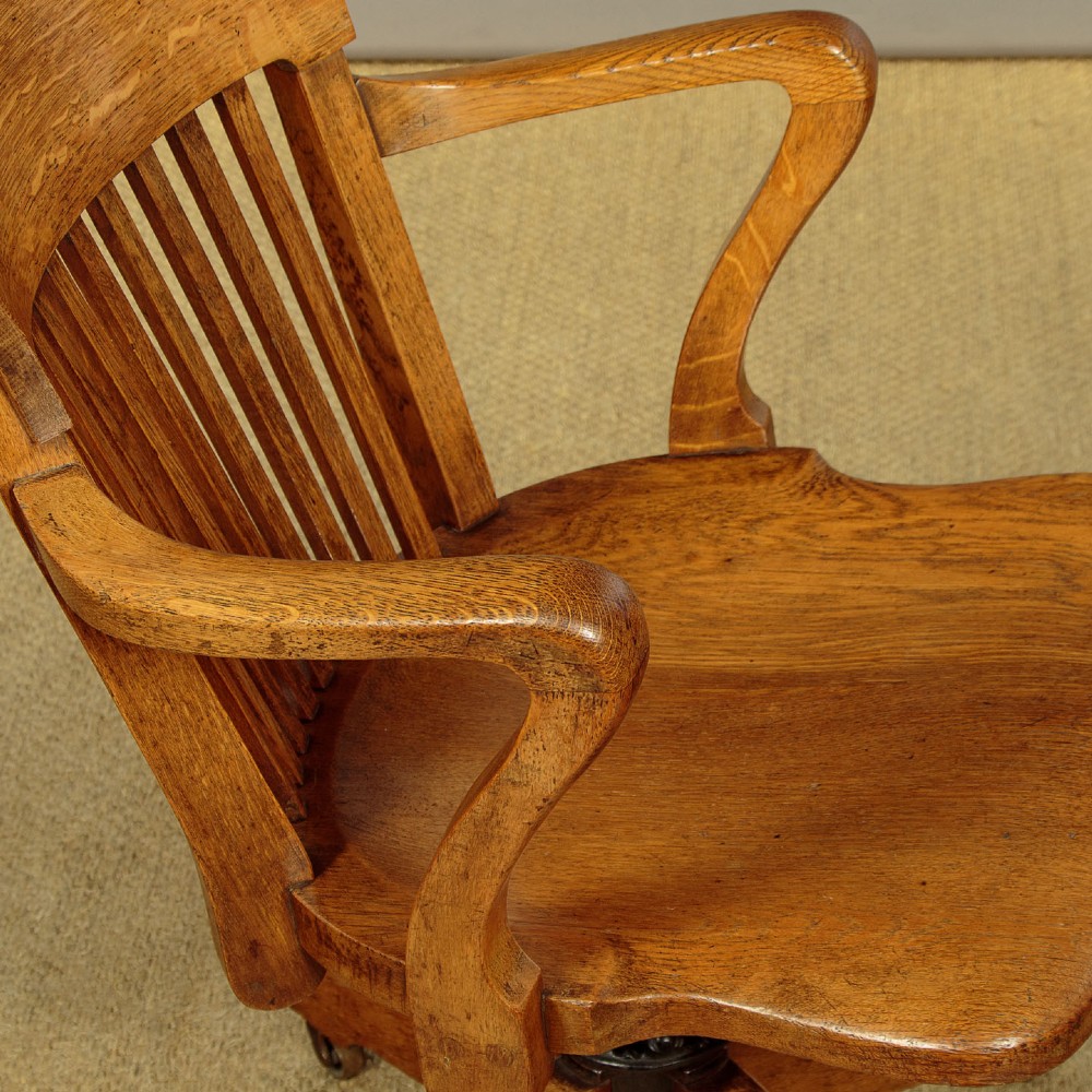 An early twentieth-century solid oak revolving desk chair featuring a slatted backrest, curved armrests, and a quadruped base on castors. View VIII