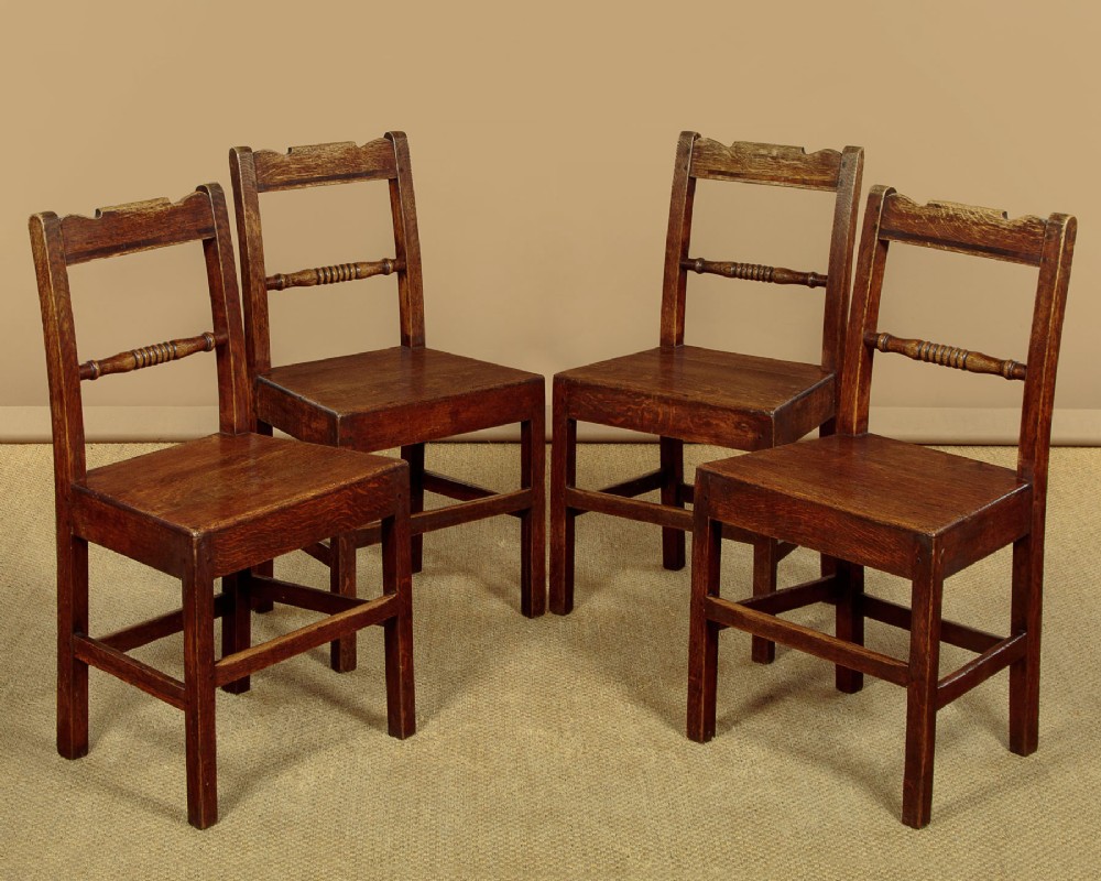 A set of four mid-19th-century Welsh oak cottage dining chairs with solid timber seats, turned centre spindles, and square stretchers.