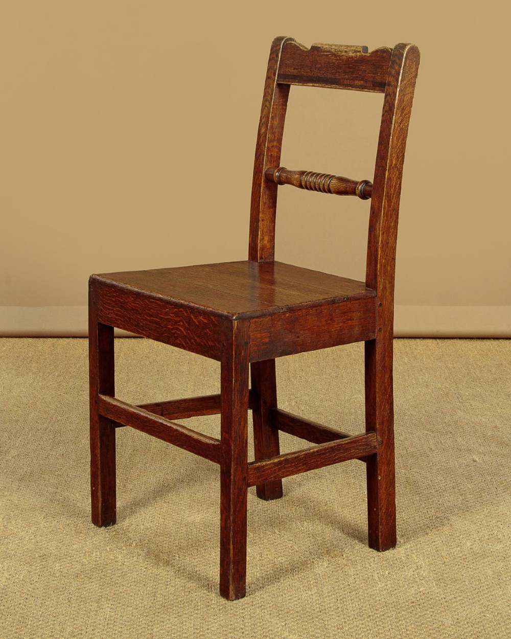 A set of four mid-19th-century Welsh oak cottage dining chairs with solid timber seats, turned centre spindles, and square stretchers. View V