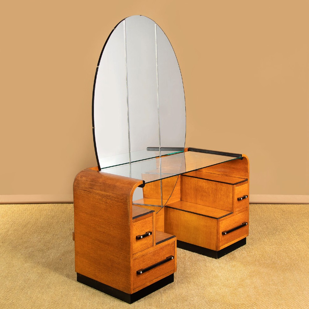 An Art Deco light oak dressing table featuring a central oval mirror, stepped drawer pedestals, and a clear glass surface. View III