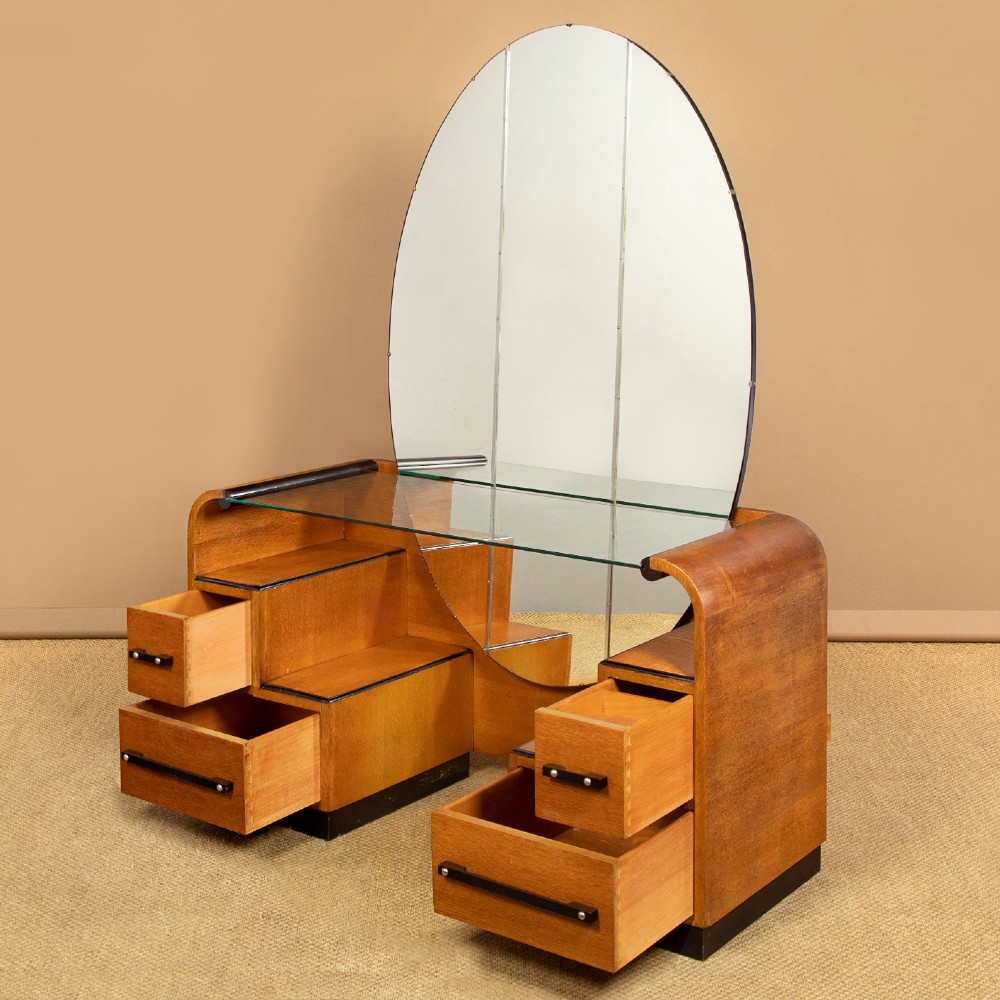 An Art Deco light oak dressing table featuring a central oval mirror, stepped drawer pedestals, and a clear glass surface. View IV