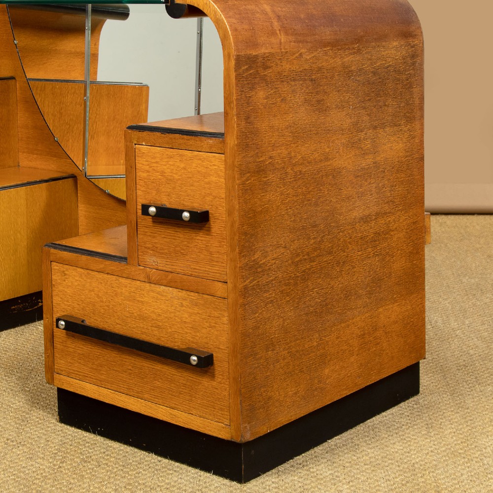 An Art Deco light oak dressing table featuring a central oval mirror, stepped drawer pedestals, and a clear glass surface. View VIII