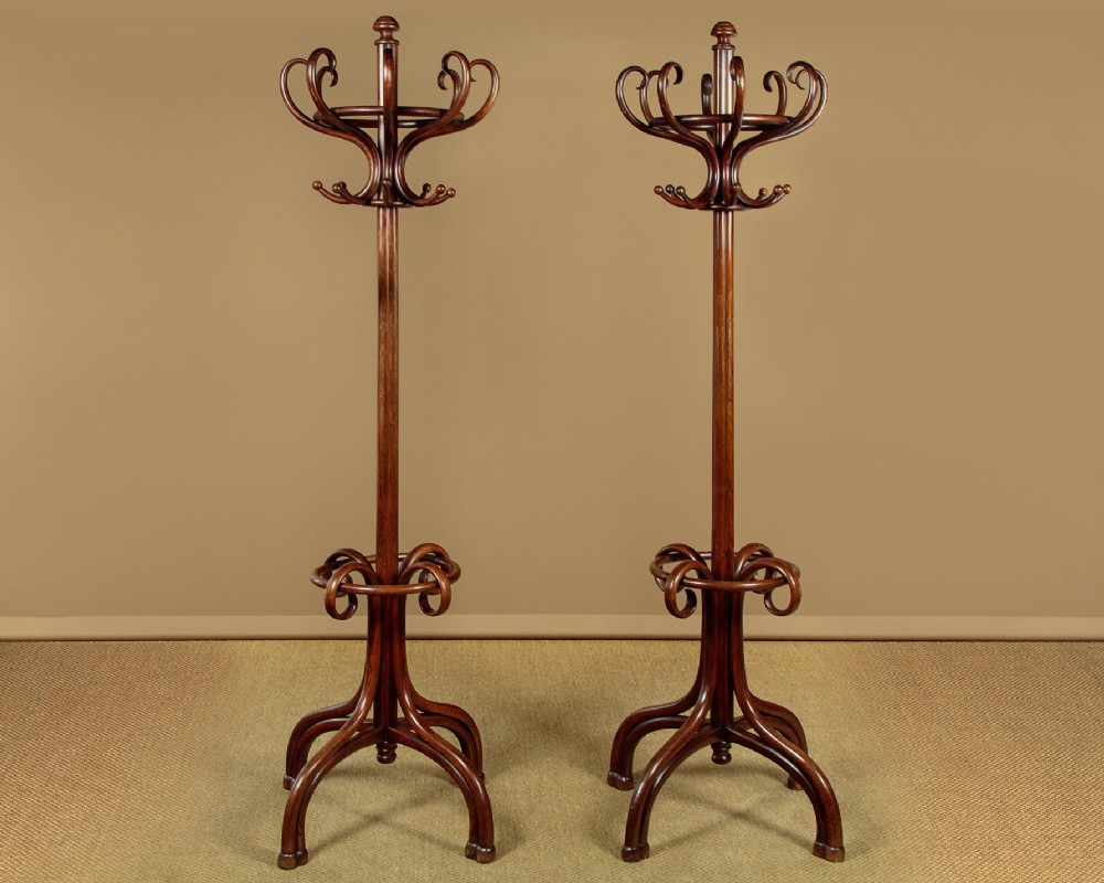 A pair of tall dark brown bentwood hallstands featuring curved coat hooks at the top and circular loops at the base for umbrellas.