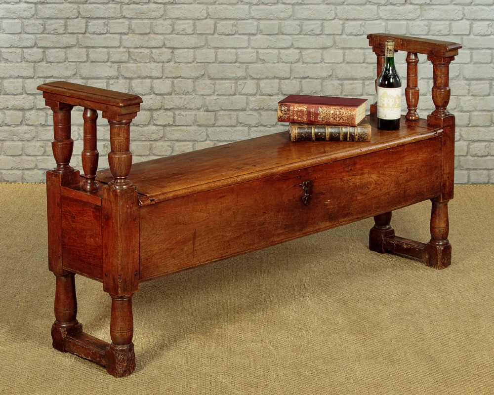 An eighteenth-century warm brown wooden box settle featuring turned end spindles, a hinged lid seat, and an iron keyhole escutcheon. View II