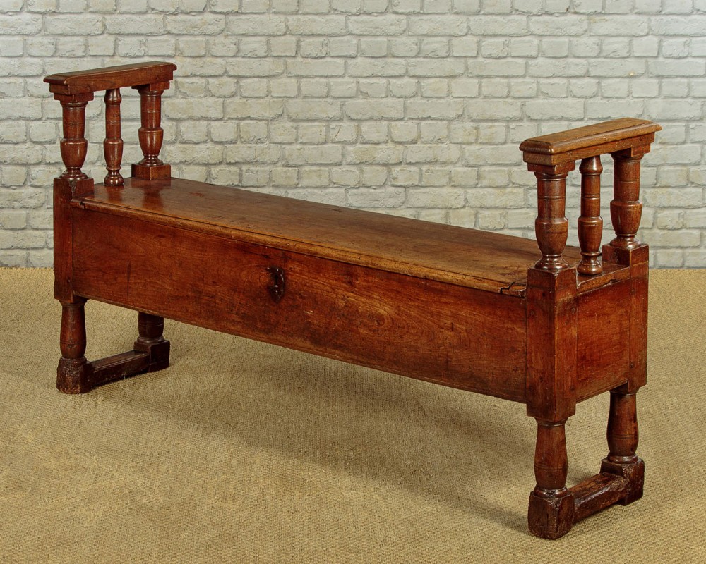 An eighteenth-century warm brown wooden box settle featuring turned end spindles, a hinged lid seat, and an iron keyhole escutcheon. View III