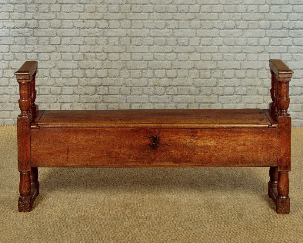 An eighteenth-century warm brown wooden box settle featuring turned end spindles, a hinged lid seat, and an iron keyhole escutcheon. View IV