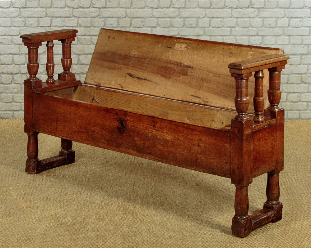An eighteenth-century warm brown wooden box settle featuring turned end spindles, a hinged lid seat, and an iron keyhole escutcheon. View V