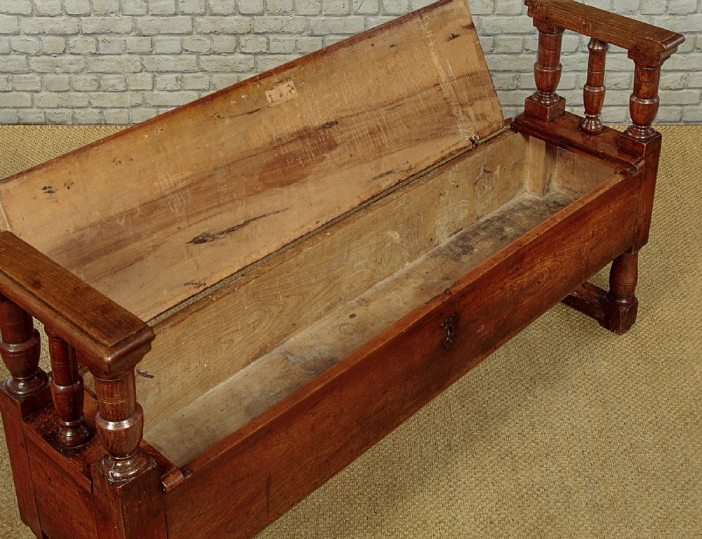 An eighteenth-century warm brown wooden box settle featuring turned end spindles, a hinged lid seat, and an iron keyhole escutcheon. View VII