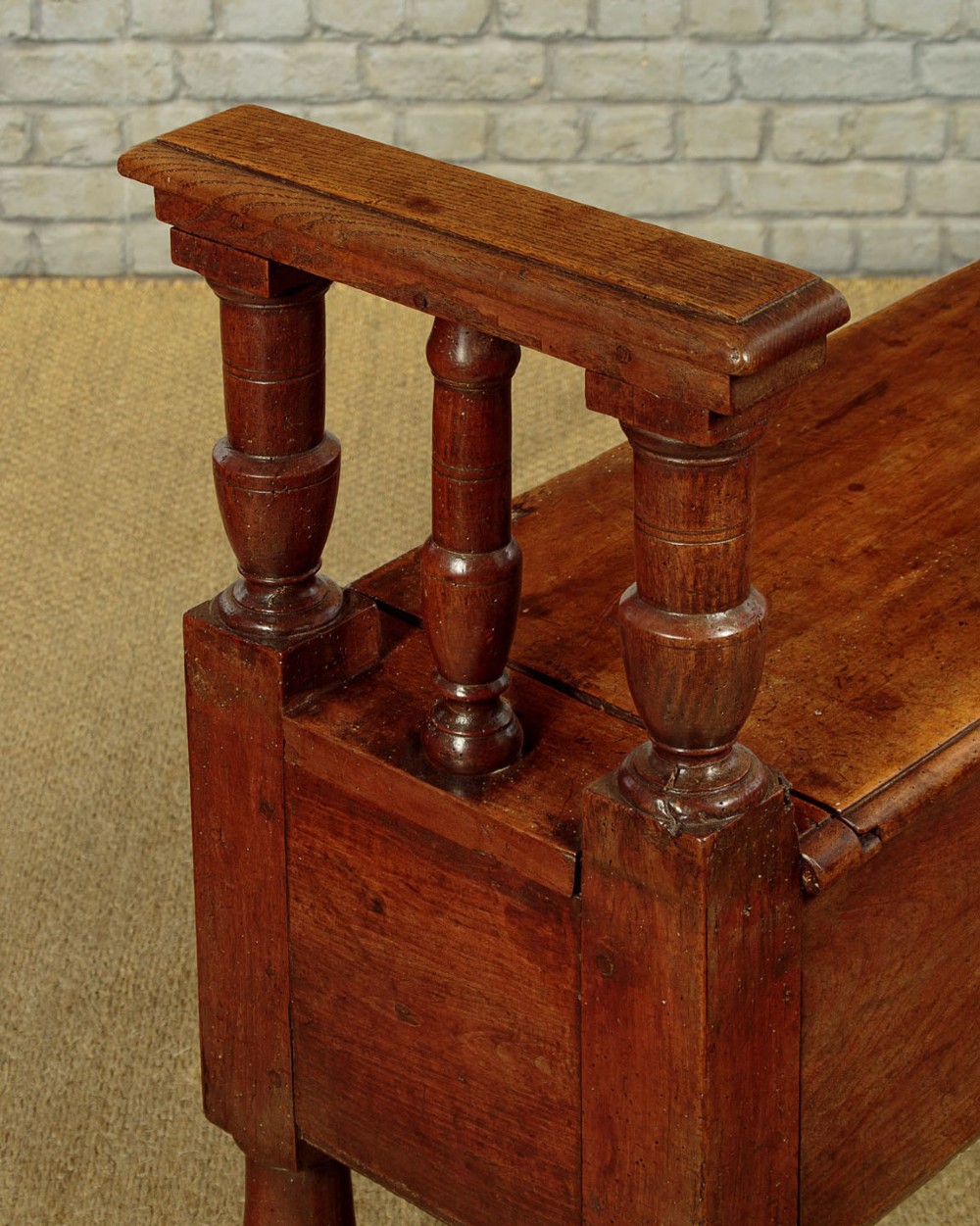 An eighteenth-century warm brown wooden box settle featuring turned end spindles, a hinged lid seat, and an iron keyhole escutcheon. View IX