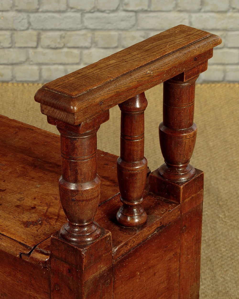 An eighteenth-century warm brown wooden box settle featuring turned end spindles, a hinged lid seat, and an iron keyhole escutcheon. View X