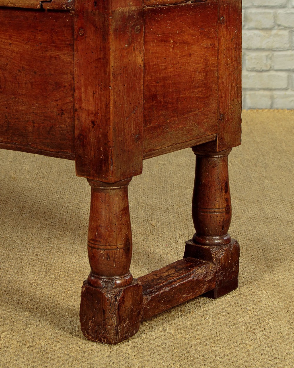 An eighteenth-century warm brown wooden box settle featuring turned end spindles, a hinged lid seat, and an iron keyhole escutcheon. View XIV