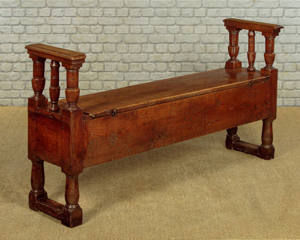 An eighteenth-century warm brown wooden box settle featuring turned end spindles, a hinged lid seat, and an iron keyhole escutcheon. View XV