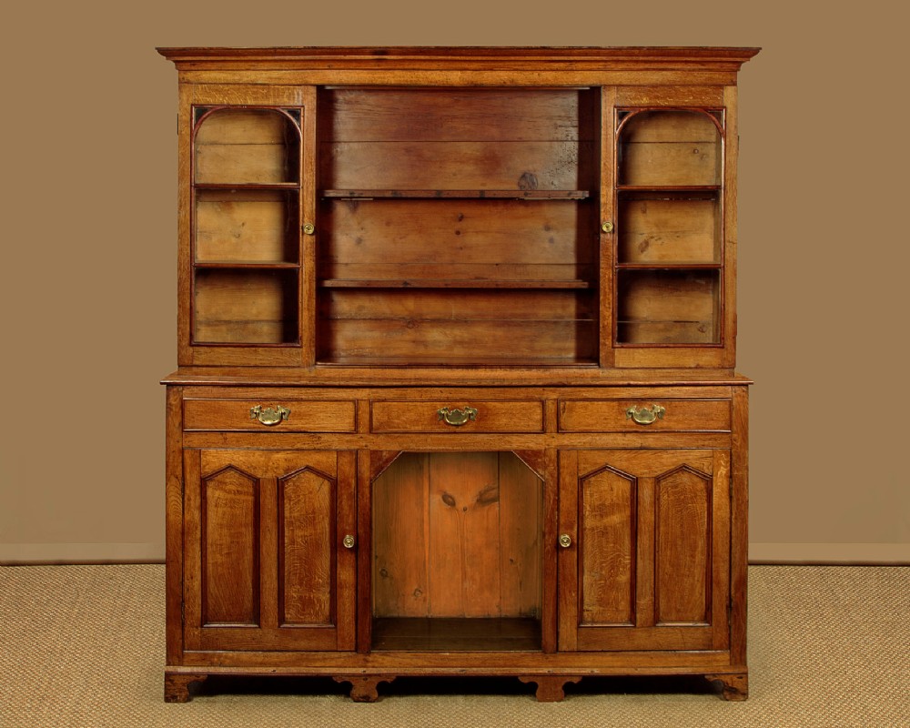 An antique nineteenth-century warm oak Welsh dog kennel dresser featuring an upper rack with glazed side cupboards above a three-drawer base with a central lower alcove.