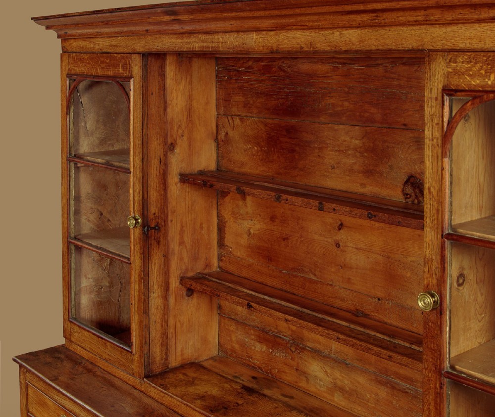 An antique nineteenth-century warm oak Welsh dog kennel dresser featuring an upper rack with glazed side cupboards above a three-drawer base with a central lower alcove. View VII