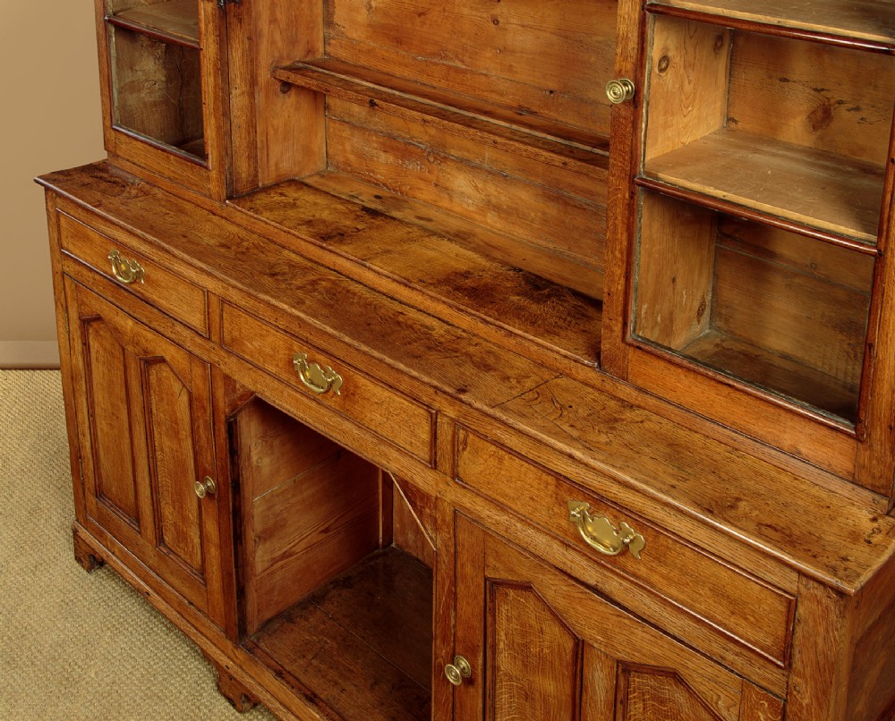 An antique nineteenth-century warm oak Welsh dog kennel dresser featuring an upper rack with glazed side cupboards above a three-drawer base with a central lower alcove. View X