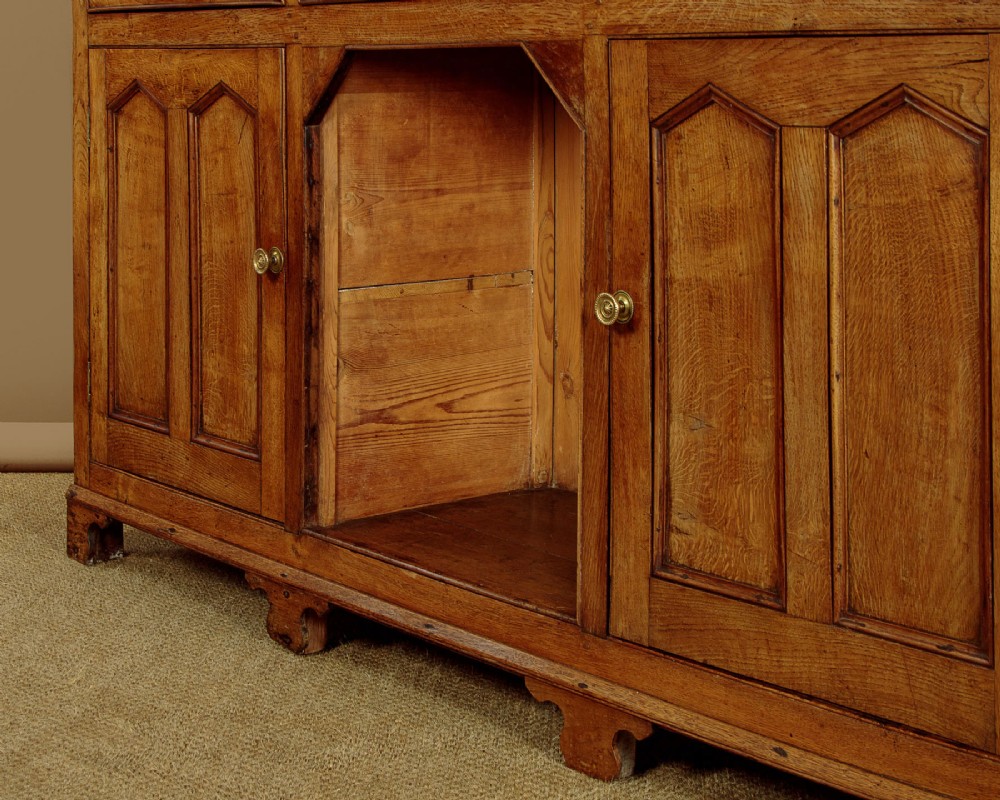 An antique nineteenth-century warm oak Welsh dog kennel dresser featuring an upper rack with glazed side cupboards above a three-drawer base with a central lower alcove. View XIII