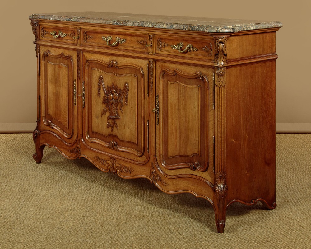 A French walnut sideboard featuring three top drawers, three panelled cabinet doors with central carved fruit motifs, brass handles, cabriole legs, and a fitted dark marble top. View II