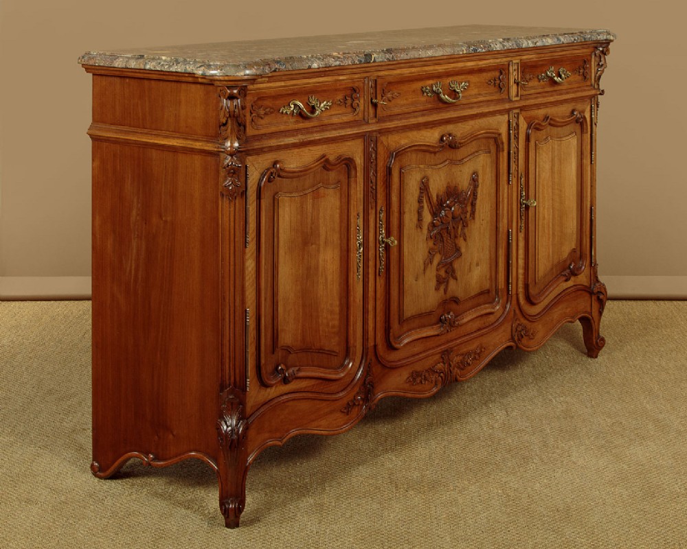 A French walnut sideboard featuring three top drawers, three panelled cabinet doors with central carved fruit motifs, brass handles, cabriole legs, and a fitted dark marble top. View III