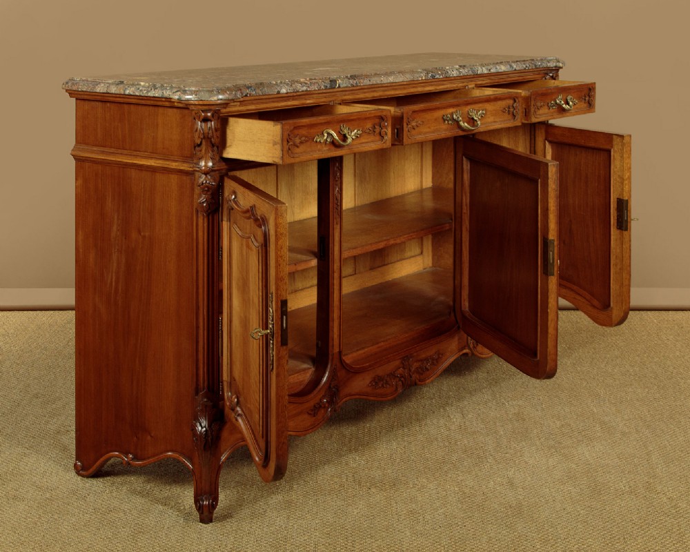 A French walnut sideboard featuring three top drawers, three panelled cabinet doors with central carved fruit motifs, brass handles, cabriole legs, and a fitted dark marble top. View IV