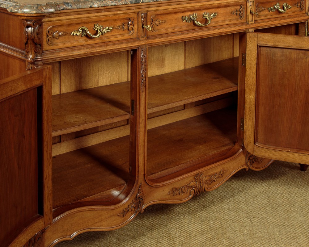 A French walnut sideboard featuring three top drawers, three panelled cabinet doors with central carved fruit motifs, brass handles, cabriole legs, and a fitted dark marble top. View XII