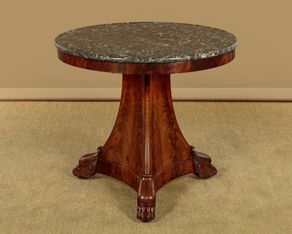 A circular antique mahogany gueridon centre table featuring a dark grey marble top, a flared central pedestal, and carved paw feet.