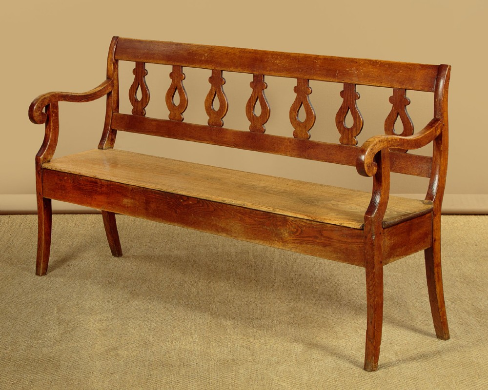 A nineteenth-century warm brown ash wooden hall bench featuring a backrest with seven pierced teardrop splats, scrolled armrests, and a solid plank seat.