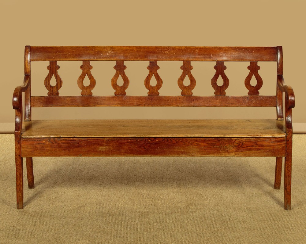 A nineteenth-century warm brown ash wooden hall bench featuring a backrest with seven pierced teardrop splats, scrolled armrests, and a solid plank seat. View II