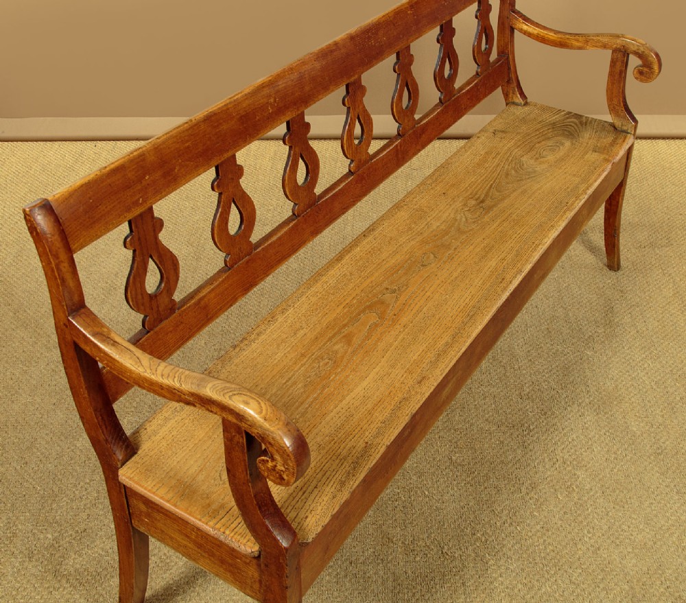 A nineteenth-century warm brown ash wooden hall bench featuring a backrest with seven pierced teardrop splats, scrolled armrests, and a solid plank seat. View III