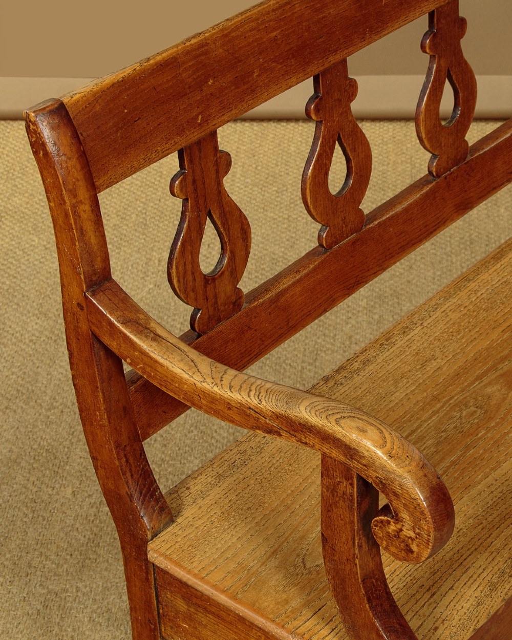 A nineteenth-century warm brown ash wooden hall bench featuring a backrest with seven pierced teardrop splats, scrolled armrests, and a solid plank seat. View IV