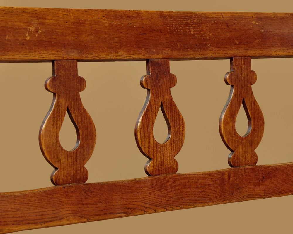 A nineteenth-century warm brown ash wooden hall bench featuring a backrest with seven pierced teardrop splats, scrolled armrests, and a solid plank seat. View V