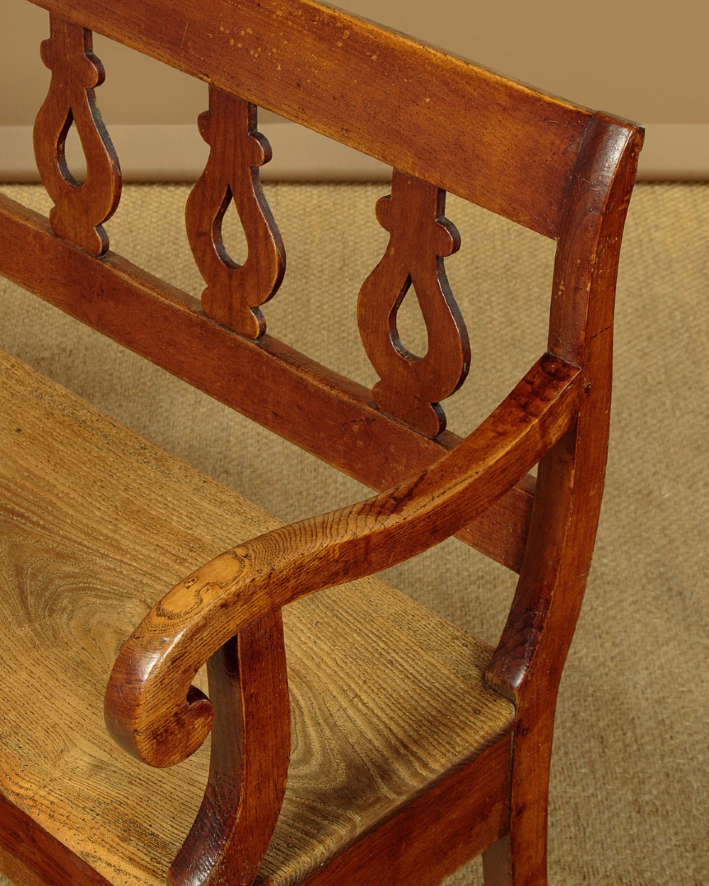 A nineteenth-century warm brown ash wooden hall bench featuring a backrest with seven pierced teardrop splats, scrolled armrests, and a solid plank seat. View VI