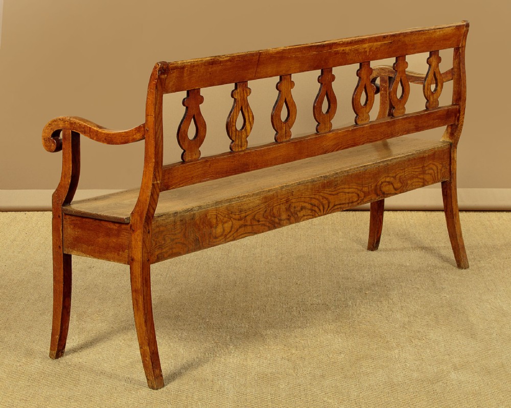 A nineteenth-century warm brown ash wooden hall bench featuring a backrest with seven pierced teardrop splats, scrolled armrests, and a solid plank seat. View VIII