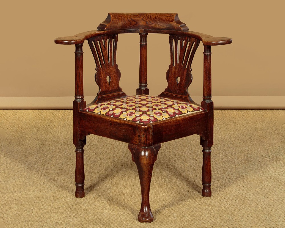 An eighteenth-century dark oak corner armchair featuring a curved top rail, two pierced splats, a patterned drop-in seat, and a central cabriole front leg.