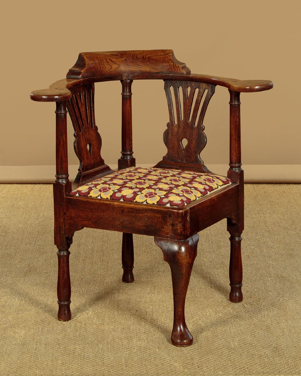 An eighteenth-century dark oak corner armchair featuring a curved top rail, two pierced splats, a patterned drop-in seat, and a central cabriole front leg. View II