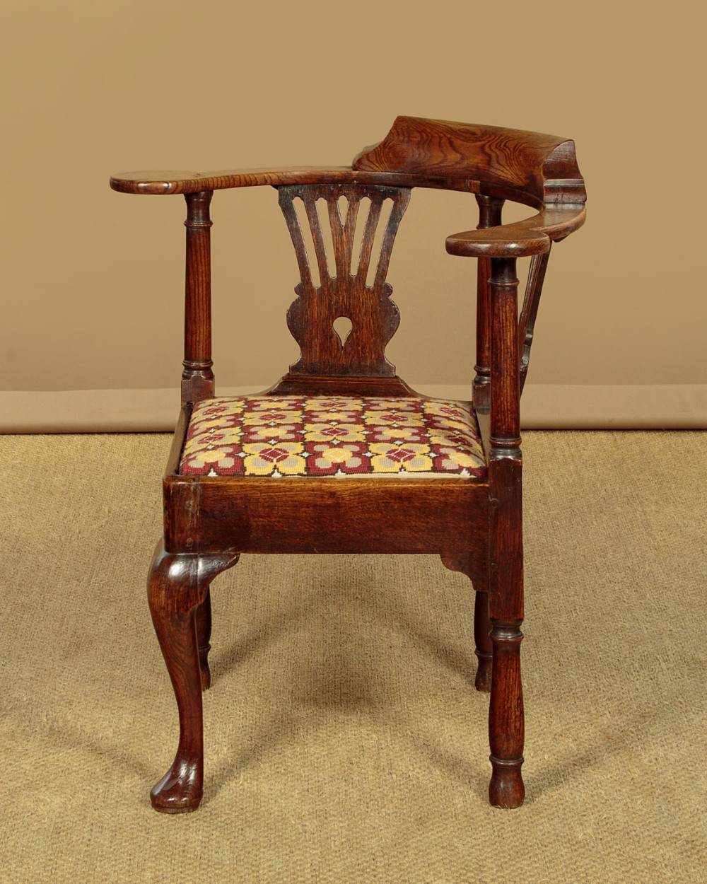 An eighteenth-century dark oak corner armchair featuring a curved top rail, two pierced splats, a patterned drop-in seat, and a central cabriole front leg. View III
