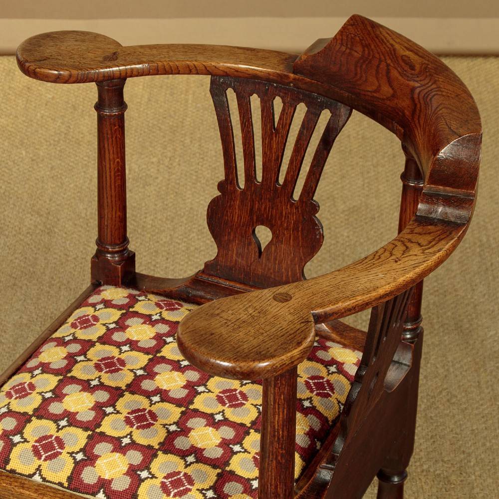 An eighteenth-century dark oak corner armchair featuring a curved top rail, two pierced splats, a patterned drop-in seat, and a central cabriole front leg. View V