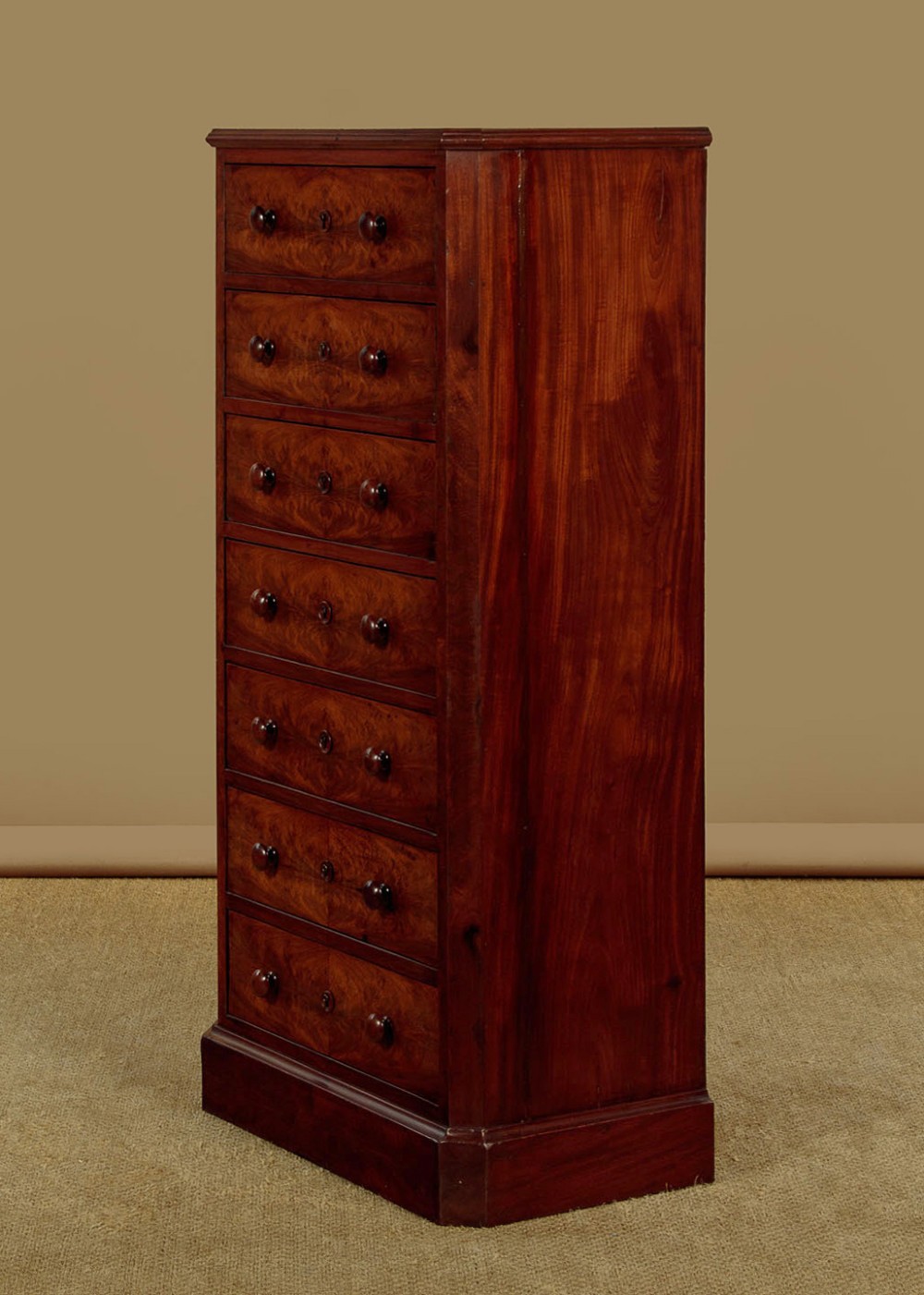 A tall and narrow Victorian mahogany bank of seven graduated drawers featuring flame mahogany veneer fronts, turned wood knob handles, and a solid plinth base. View III
