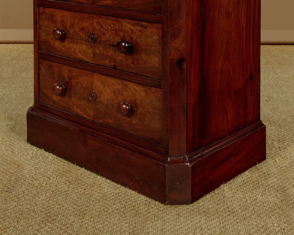 A tall and narrow Victorian mahogany bank of seven graduated drawers featuring flame mahogany veneer fronts, turned wood knob handles, and a solid plinth base. View IX