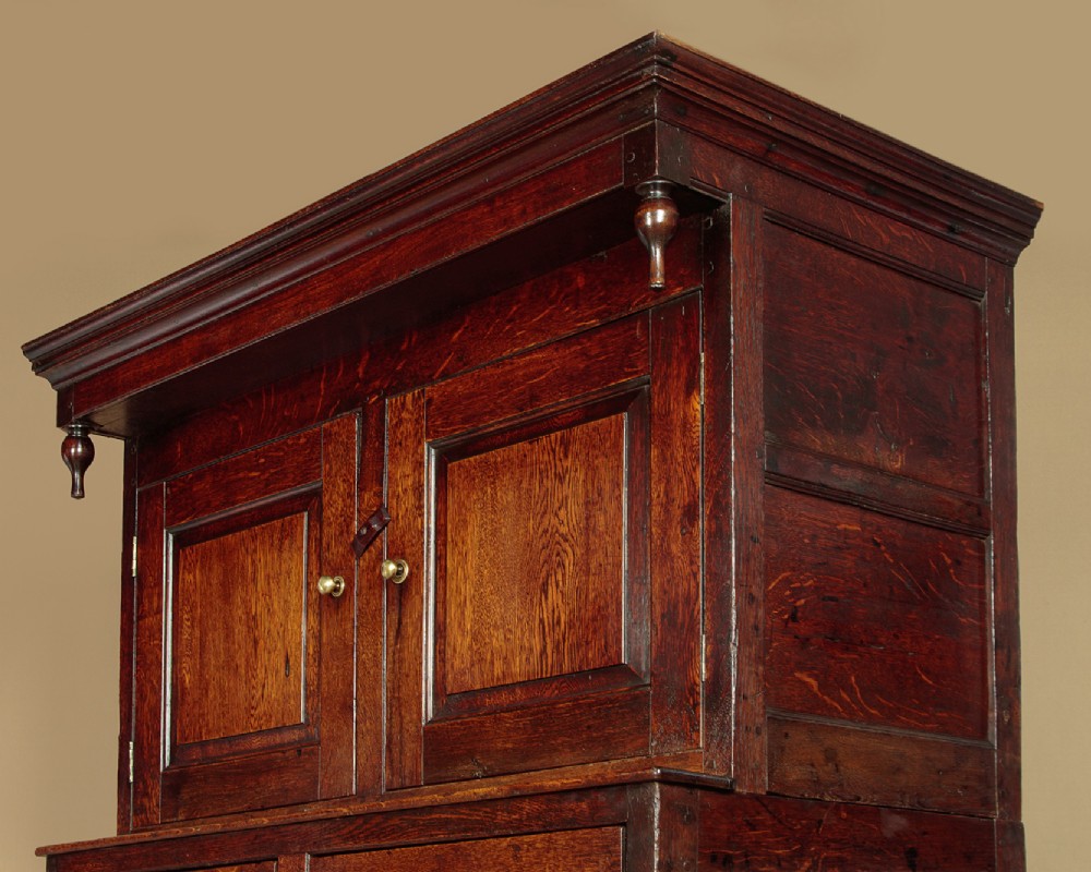 An 18th-century dark Welsh oak cwpwrdd deuddarn featuring an overhanging canopy with drop pendants, upper fielded panel doors, two drawers, and lower cupboard doors. View V
