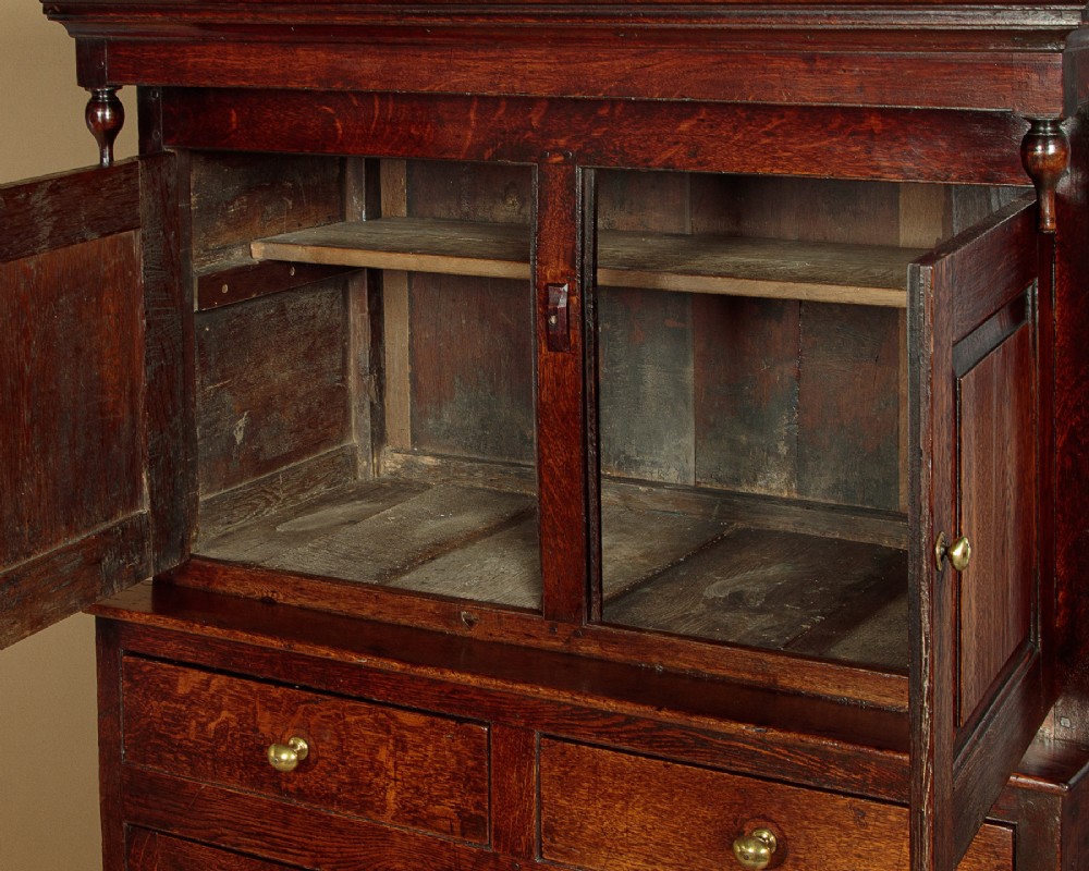 An 18th-century dark Welsh oak cwpwrdd deuddarn featuring an overhanging canopy with drop pendants, upper fielded panel doors, two drawers, and lower cupboard doors. View VII