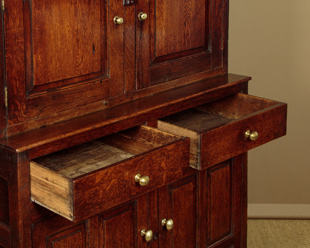 An 18th-century dark Welsh oak cwpwrdd deuddarn featuring an overhanging canopy with drop pendants, upper fielded panel doors, two drawers, and lower cupboard doors. View VIII
