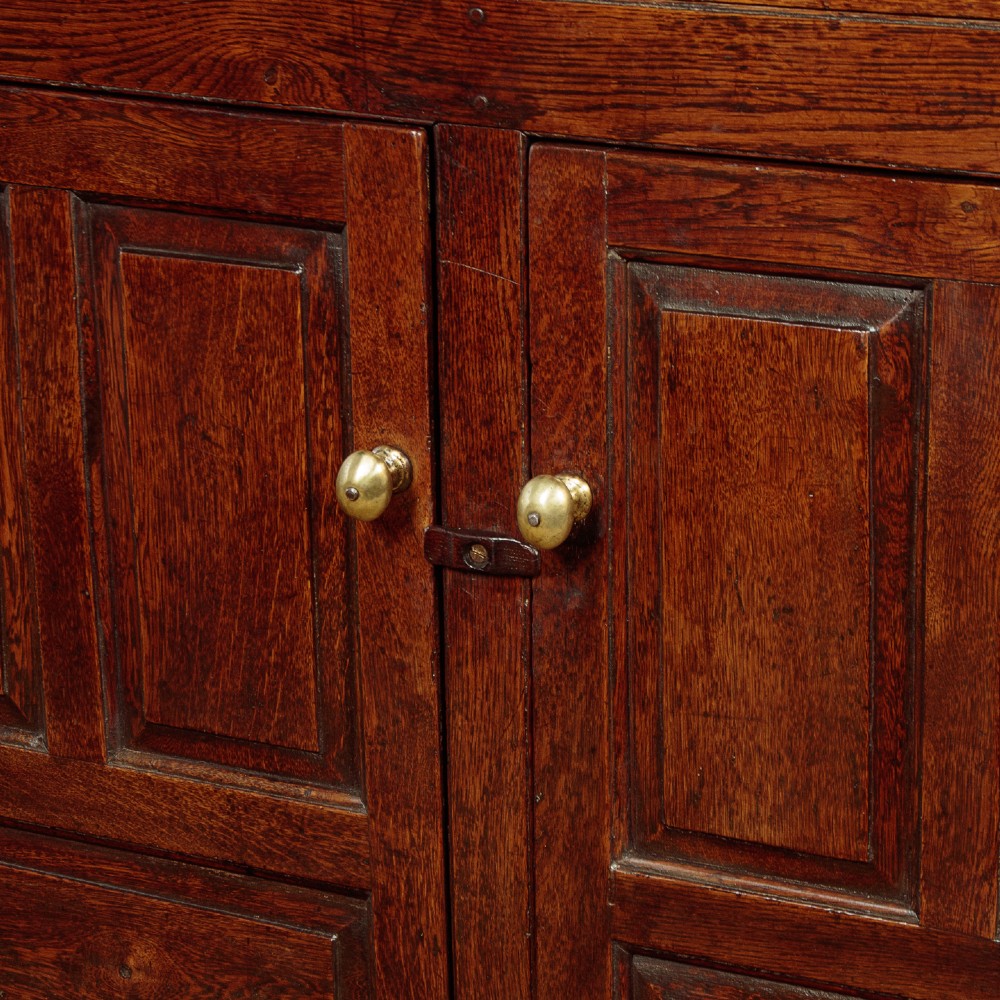 An 18th-century dark Welsh oak cwpwrdd deuddarn featuring an overhanging canopy with drop pendants, upper fielded panel doors, two drawers, and lower cupboard doors. View IX