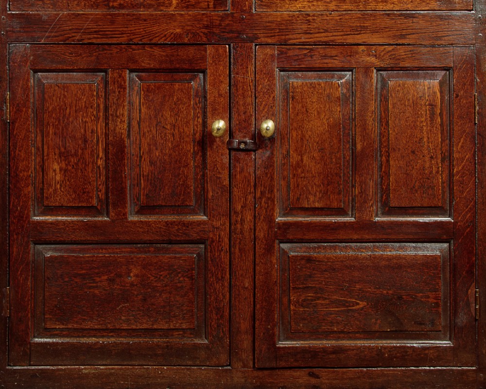 An 18th-century dark Welsh oak cwpwrdd deuddarn featuring an overhanging canopy with drop pendants, upper fielded panel doors, two drawers, and lower cupboard doors. View X