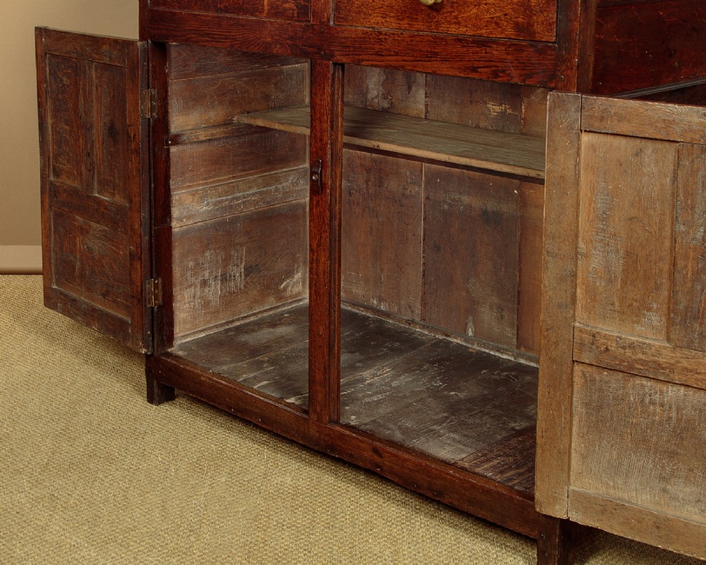 An 18th-century dark Welsh oak cwpwrdd deuddarn featuring an overhanging canopy with drop pendants, upper fielded panel doors, two drawers, and lower cupboard doors. View XI