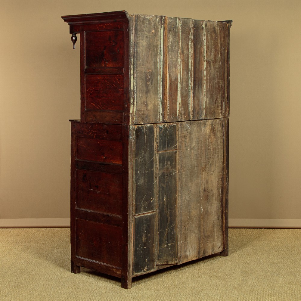 An 18th-century dark Welsh oak cwpwrdd deuddarn featuring an overhanging canopy with drop pendants, upper fielded panel doors, two drawers, and lower cupboard doors. View XIII