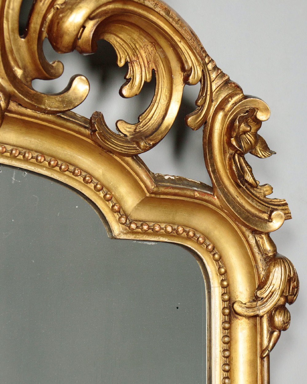 A large late Victorian giltwood overmantel mirror with an arched top, detailed beaded inner rim, and carved cresting featuring acanthus scrollwork. View V
