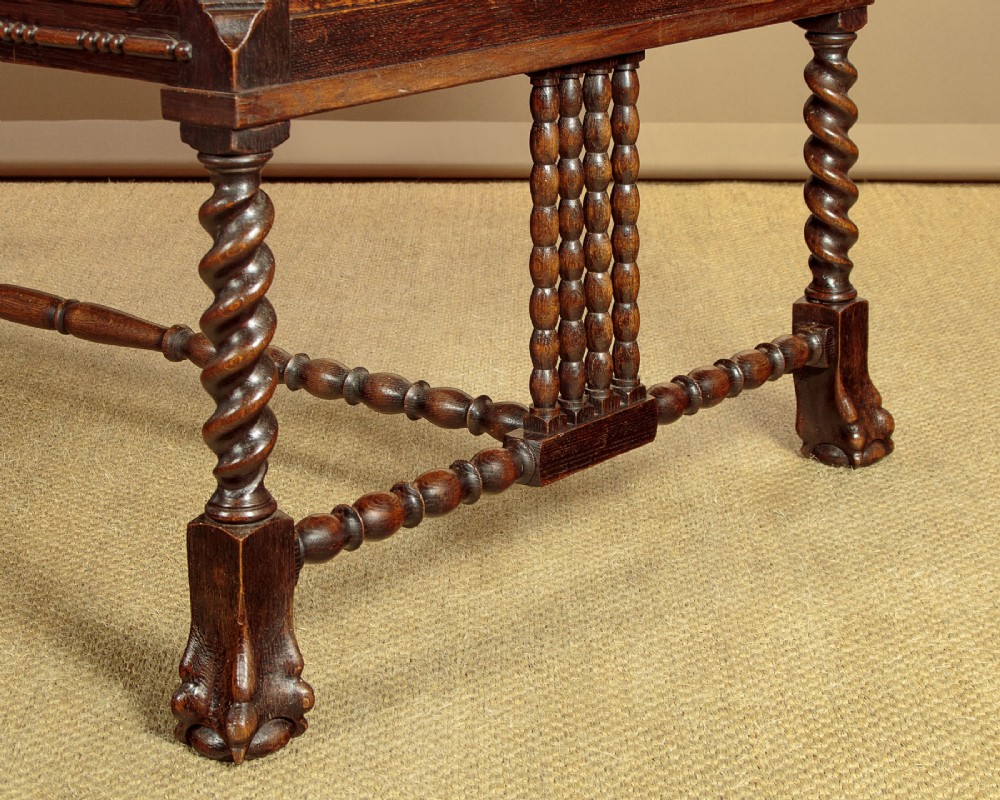 A dark carved oak writing desk featuring four geometric drawers, a scroll-carved central frieze, barley-twist legs, and a stretcher base. View X