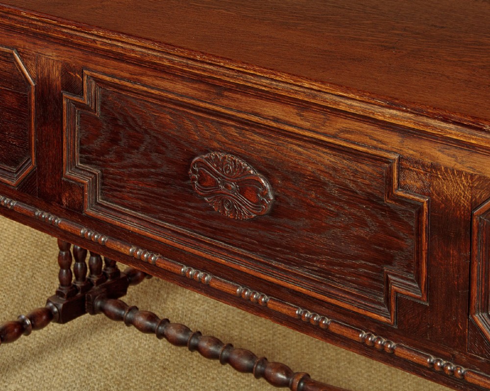 A dark carved oak writing desk featuring four geometric drawers, a scroll-carved central frieze, barley-twist legs, and a stretcher base. View XIII