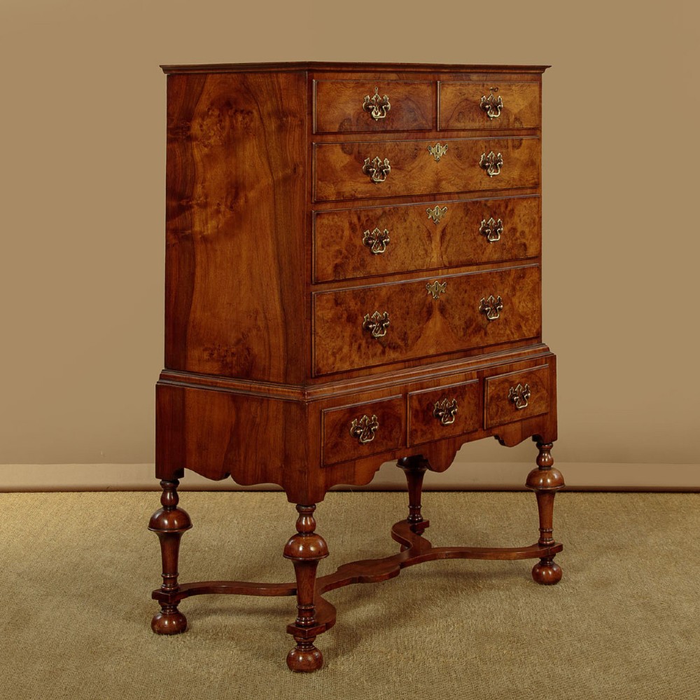 A 1930s Queen Anne Revival burr walnut chest on stand featuring multiple graduated drawers, decorative brass handles, turned legs, and a shaped apron. View II